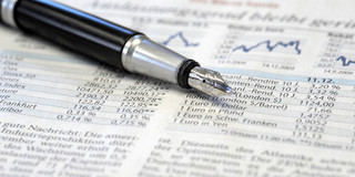 A newspaper with information about the stock exchange and a fountain pen lie on top.